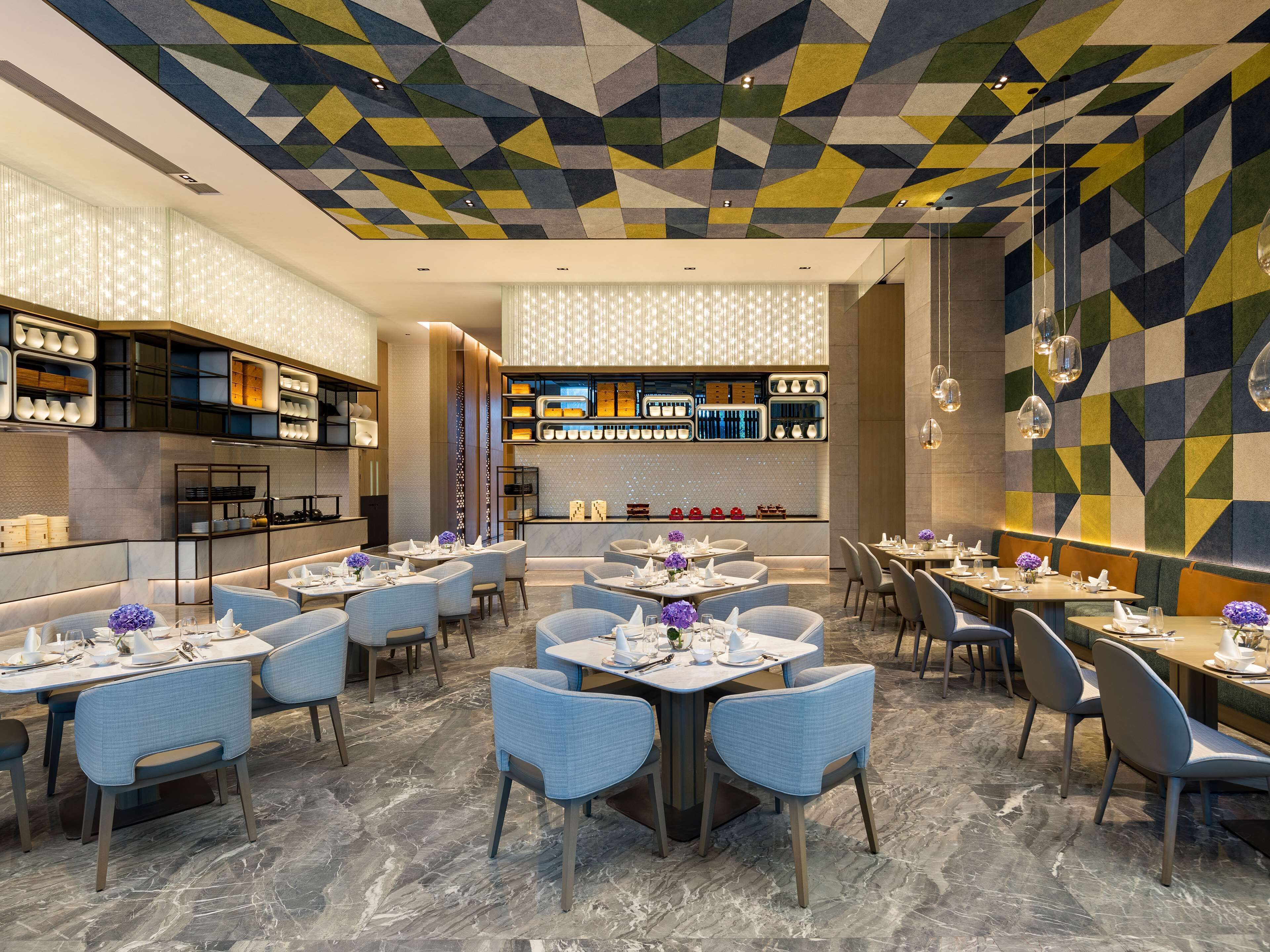 Un restaurante moderno con techo de patrón geométrico, suelo de mármol y mesas y sillas ordenadas.