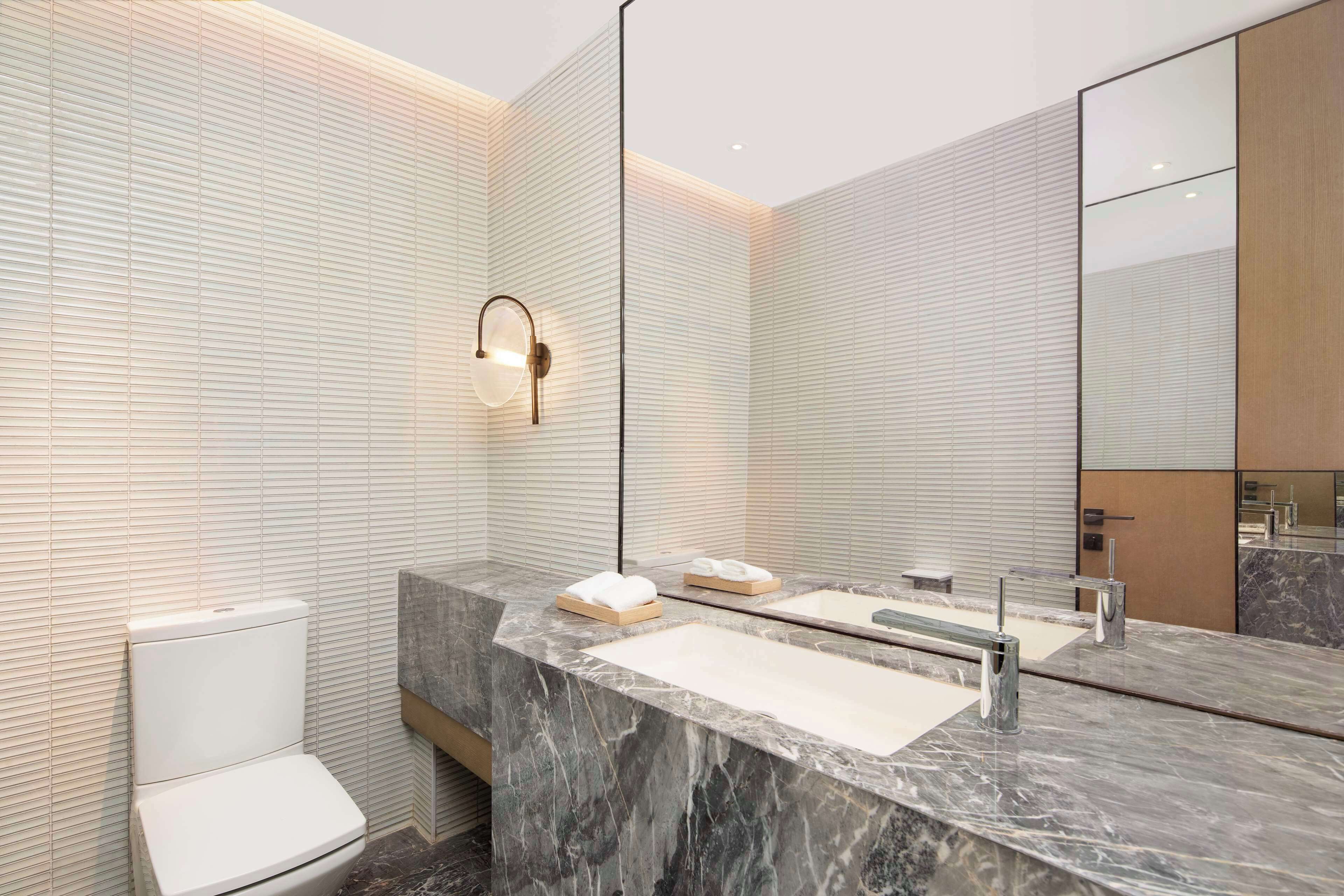 A modern bathroom with a marble vanity, a toilet, and a large mirror.
