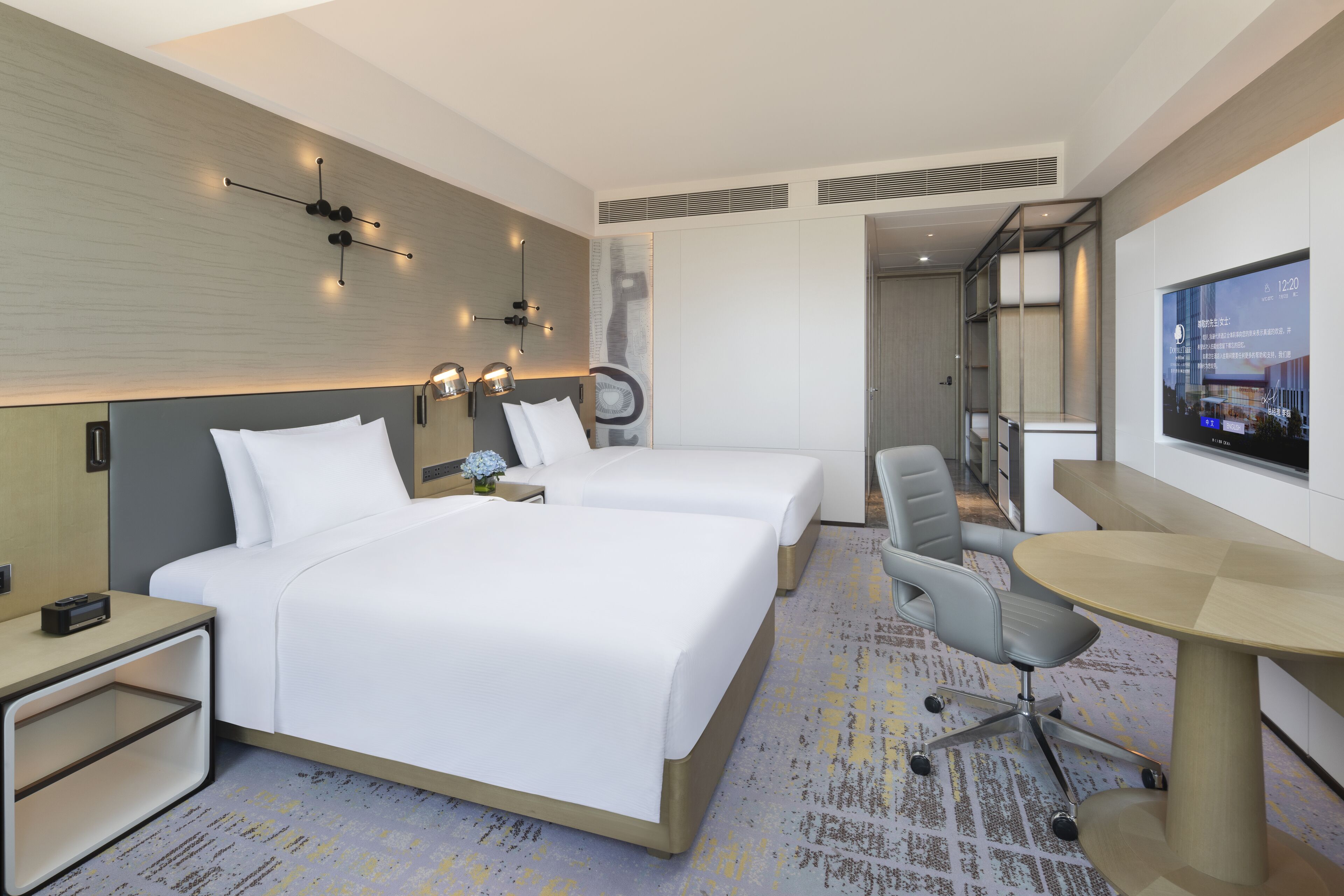 A hotel room with two beds, a desk, and a TV.
