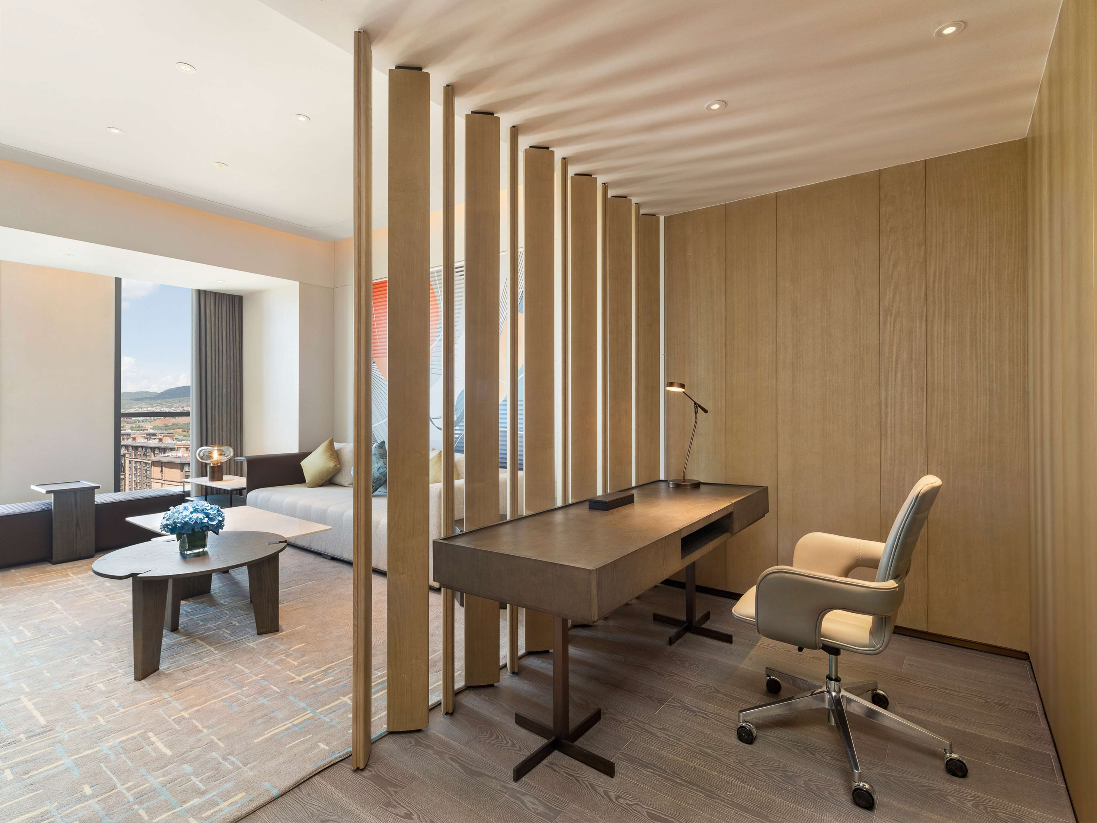 A modern office space with a long table, a high chair, and a view of the city through large windows.