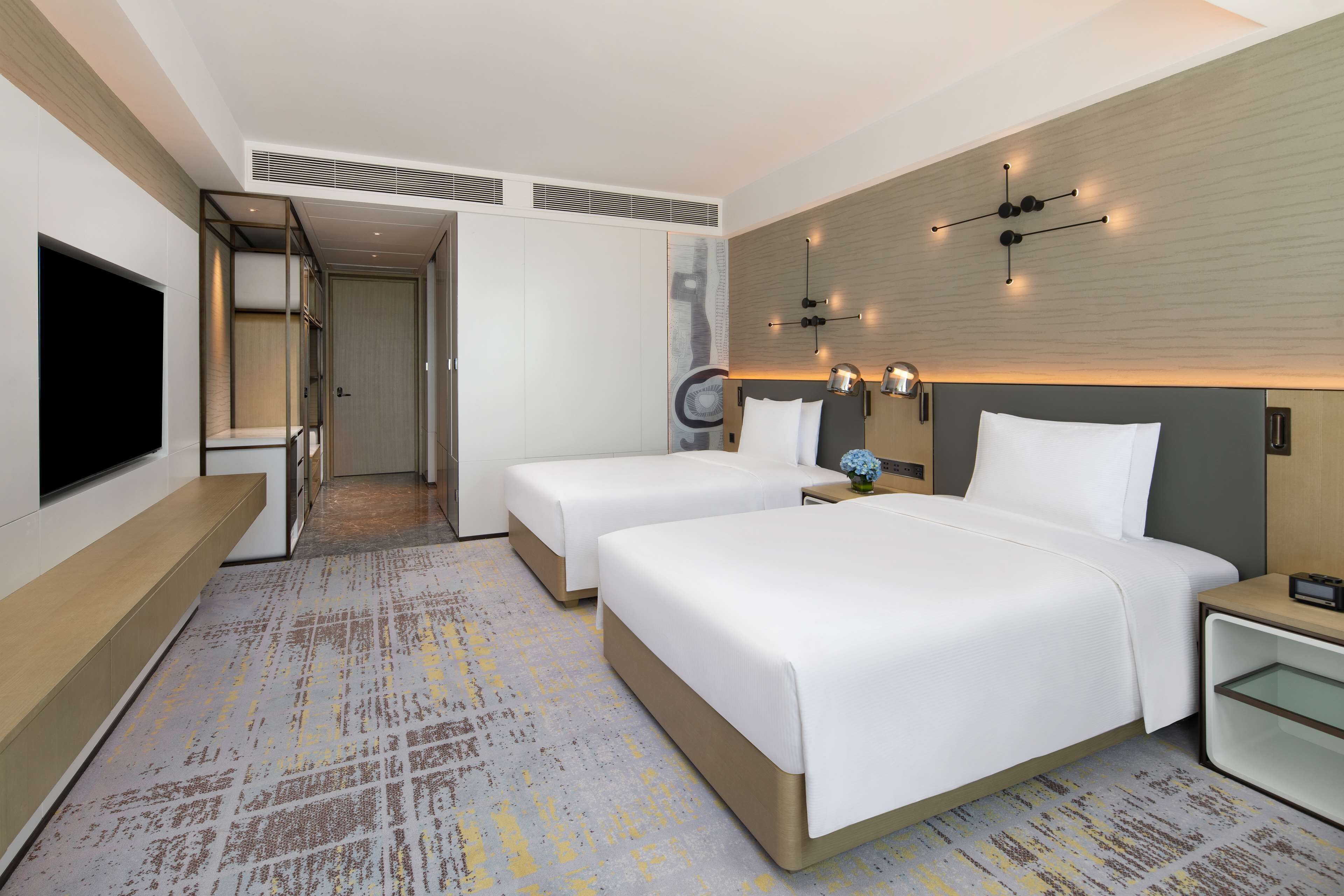 Een moderne hotelkamer met twee bedden, een flatscreen televisie, een nachtkastje met een lamp en een wandlamp.