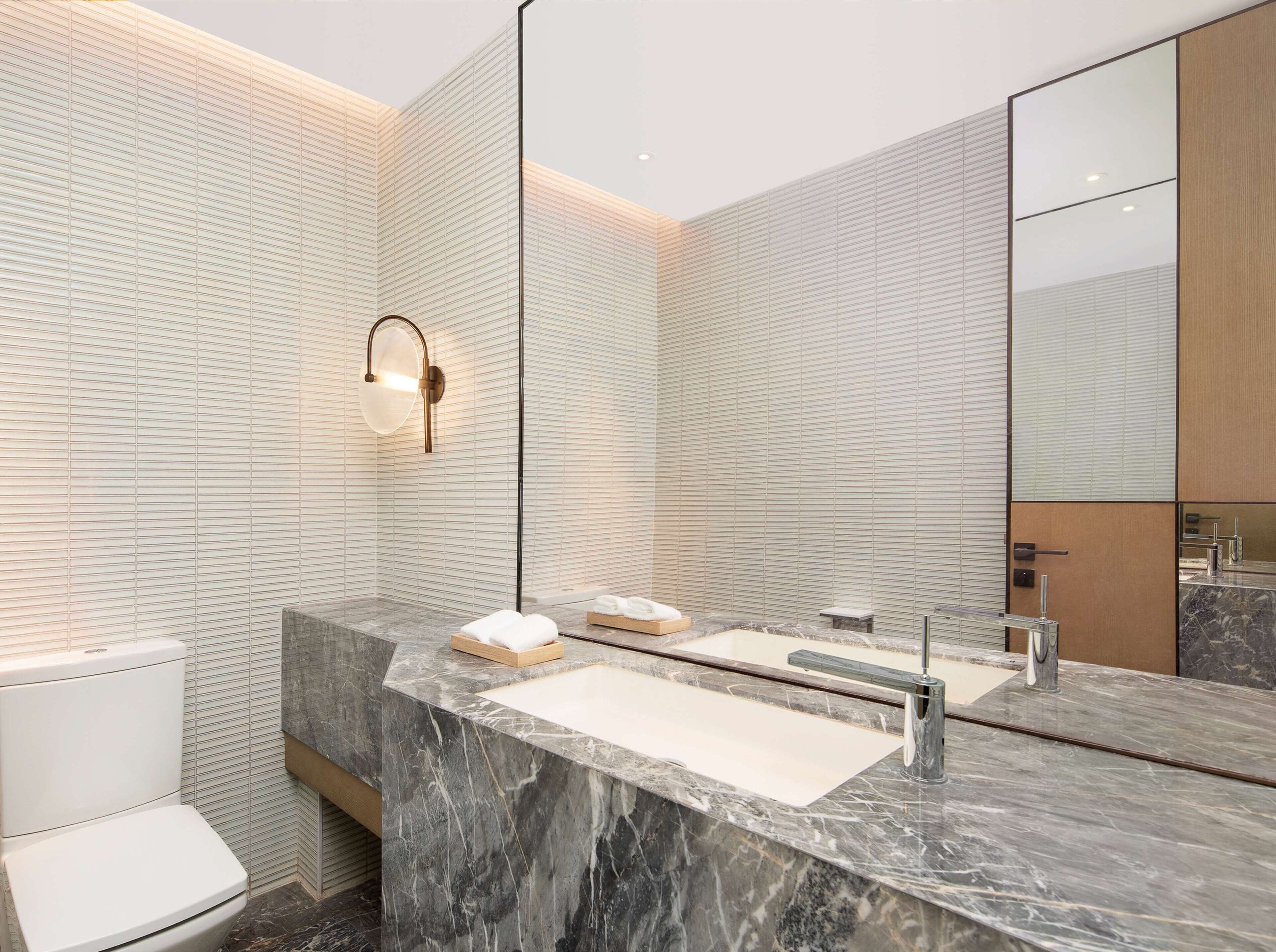 A modern bathroom with a marble vanity, a large mirror, and a toilet.