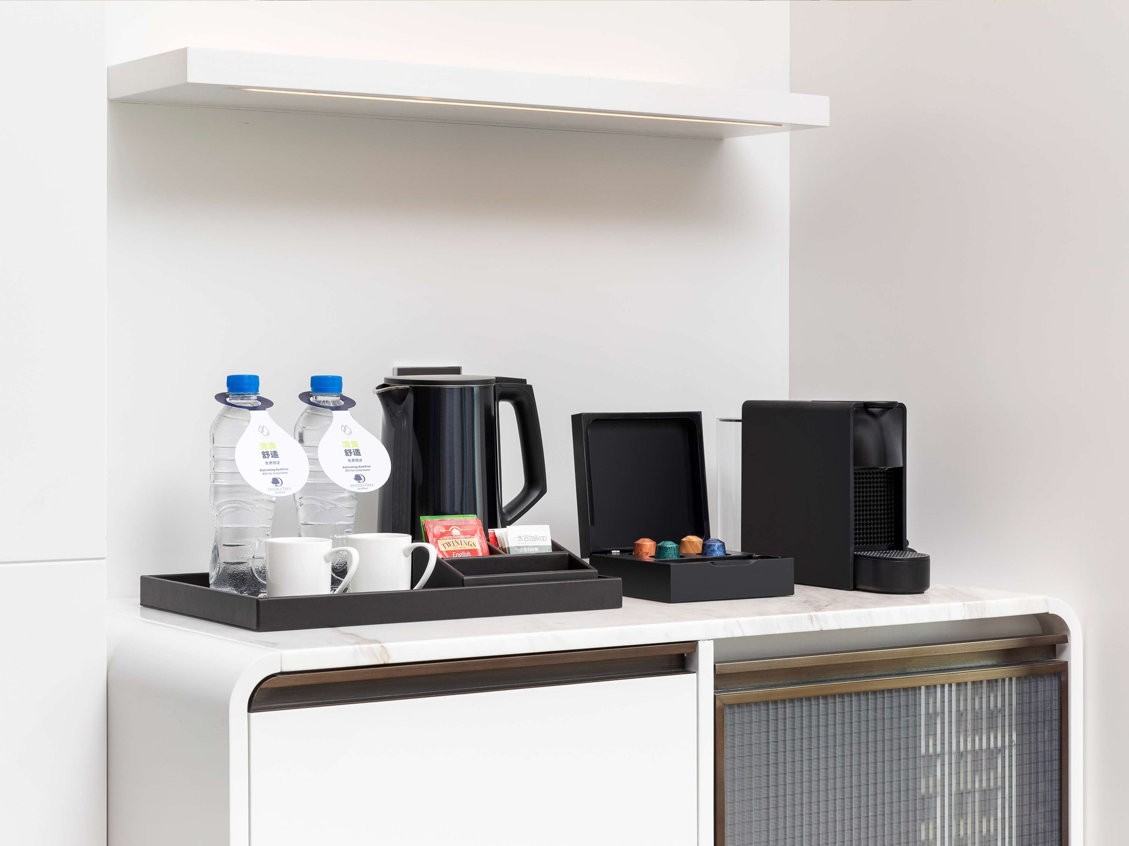 Um espaço com café, incluindo duas garrafas de água, uma cafeteira, um bule de chá e uma caixa de saquinhos de chá.