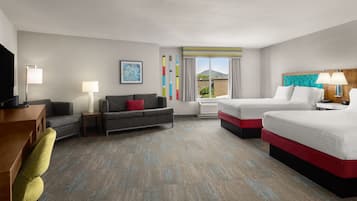 Quarto de hotel com escrivaninha, duas camas, um sofá e uma televisão.