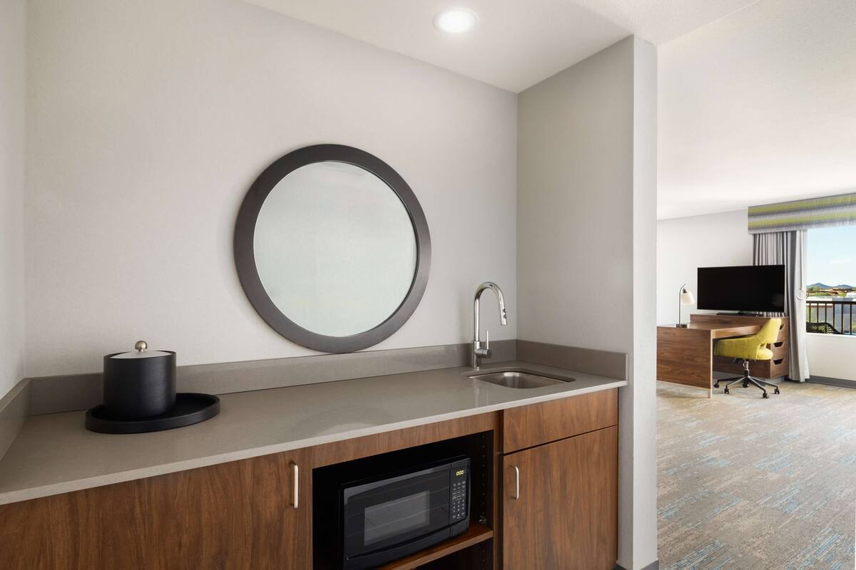 A modern kitchen with a microwave, sink, and a round mirror on the wall.