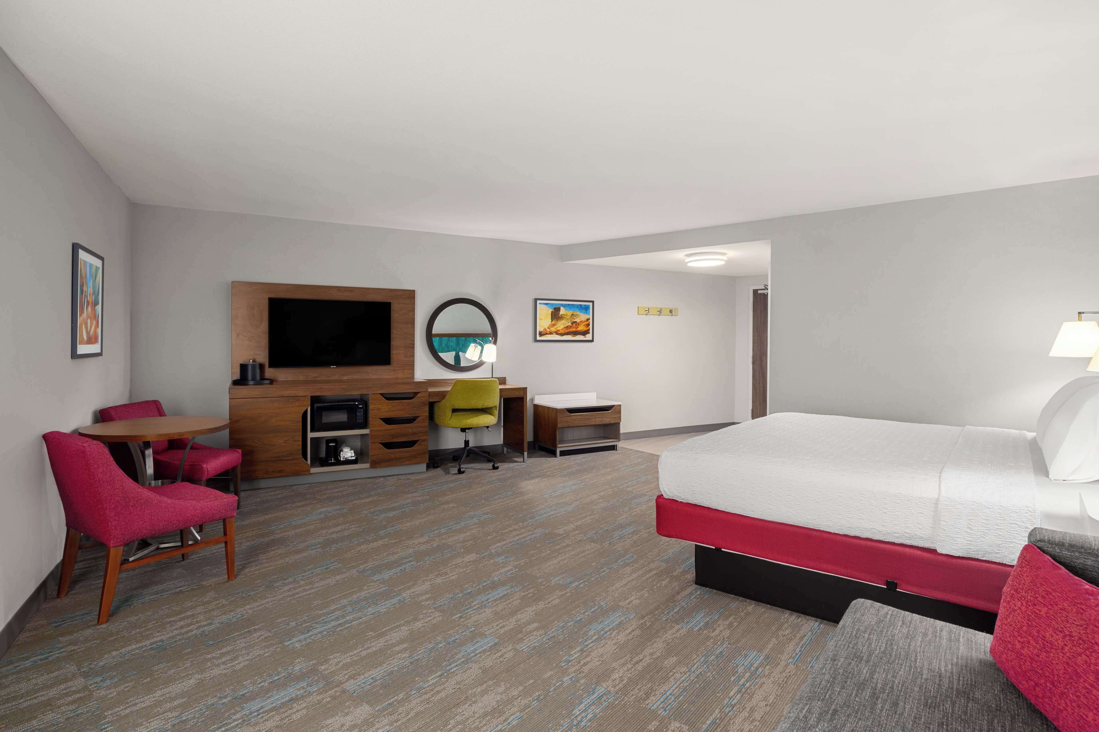 A hotel room with a bed, a desk, a chair, a TV, and a small table.
