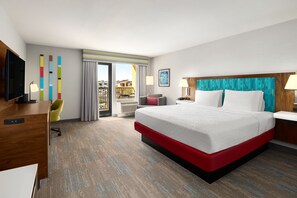 A hotel room with a large bed, a desk, a chair, a TV, and a balcony with a view.