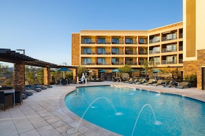 A hotel with a swimming pool, outdoor seating, and a multi-story building.