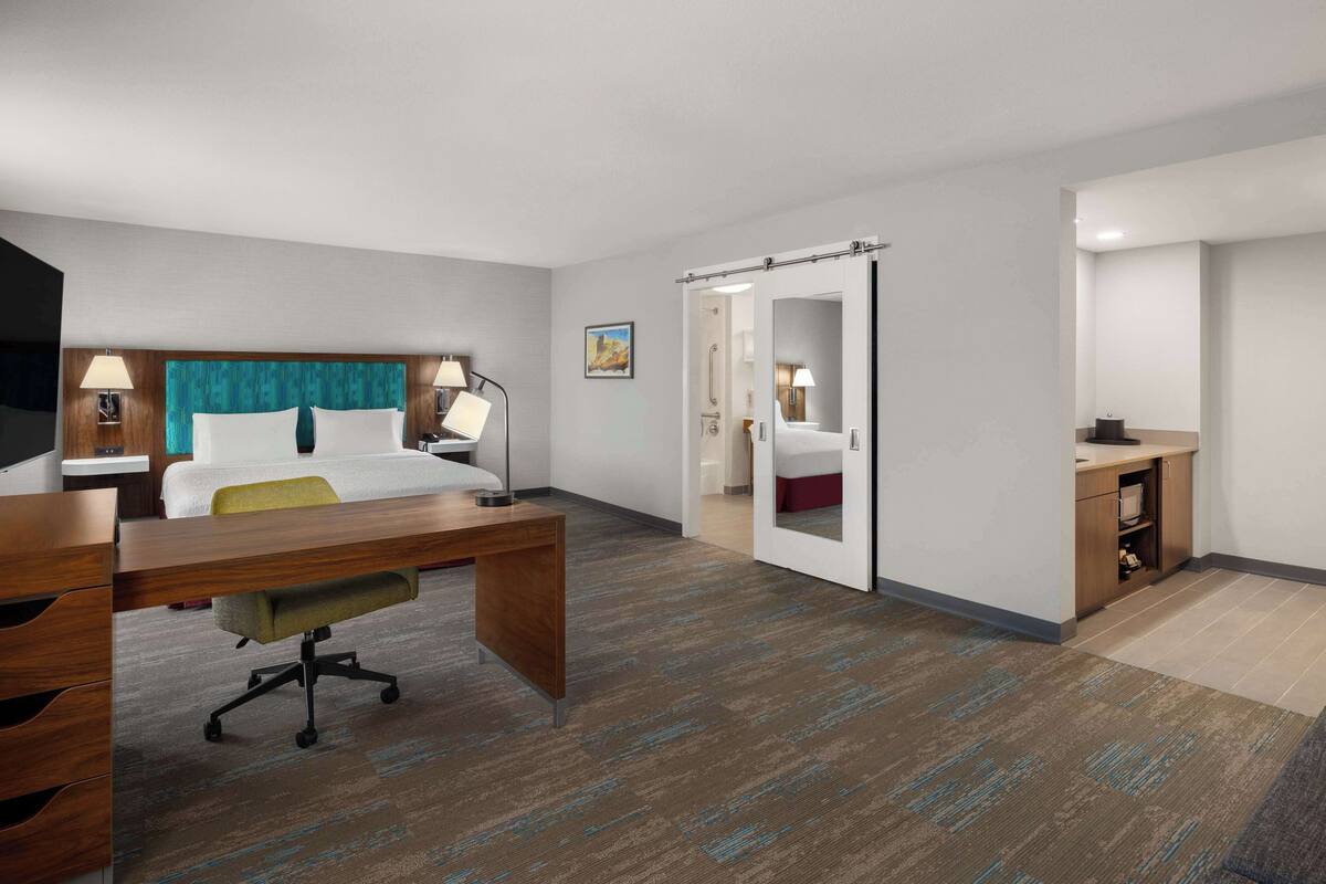 A hotel room with a bed, desk, chair, and a small kitchenette.