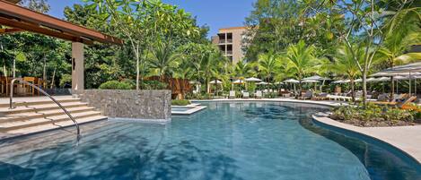 A swimming pool with a curved design, surrounded by palm trees and lounge chairs.