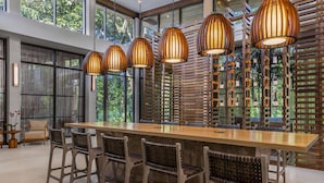 A modern bar area with a long wooden counter, wicker chairs, and hanging pendant lights. - Botanika Osa Peninsula Resort, Curio Collection by Hilton (Puerto Jiménez)