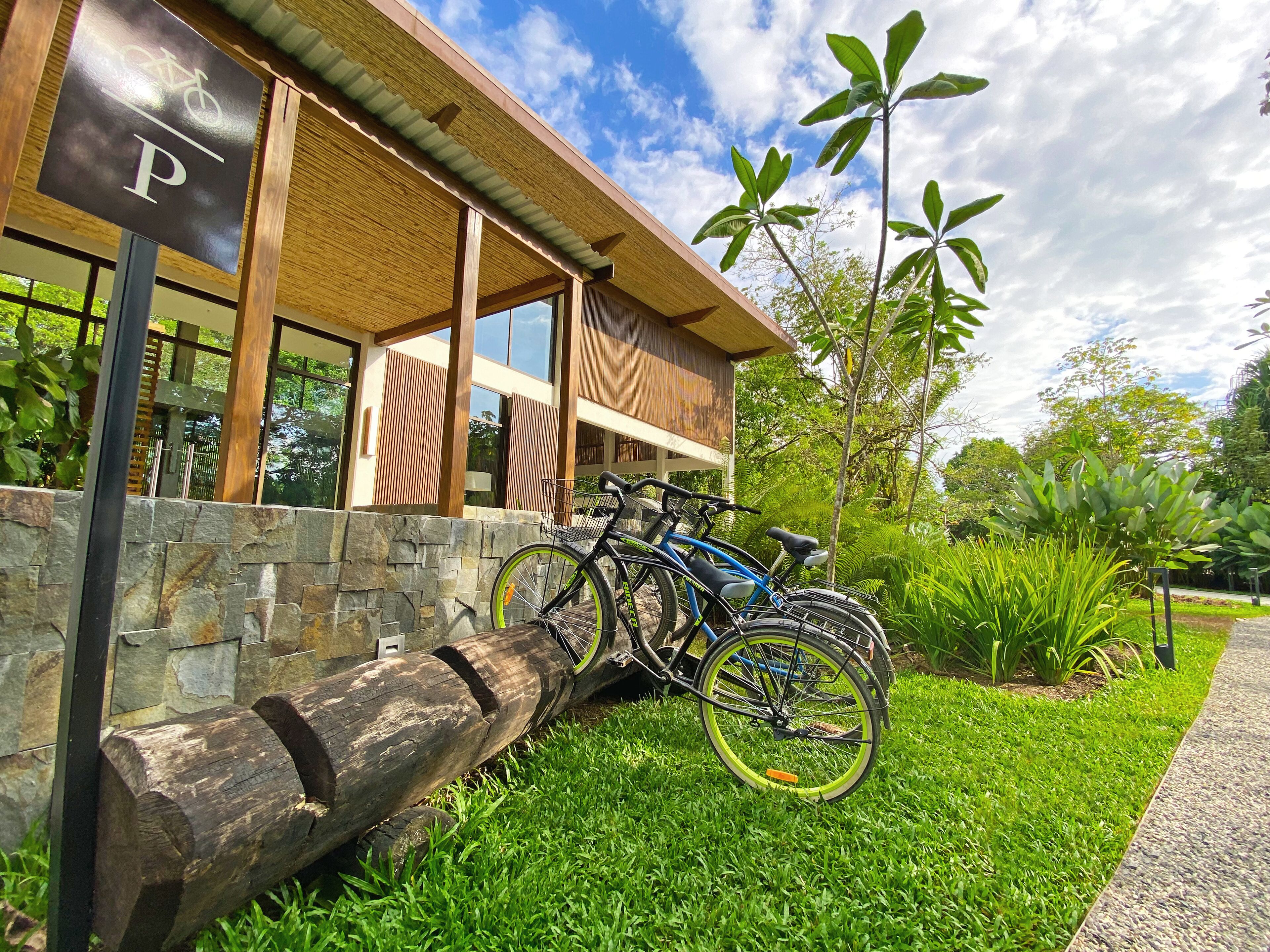 A modern building with a bike rack outside, a stone wall, and lush greenery.