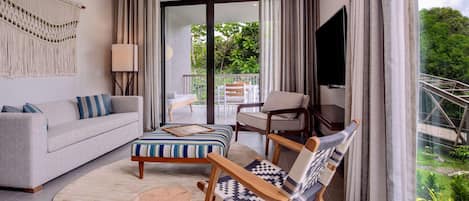A modern living room with a sofa, a patterned ottoman, a wooden side table, and a chair with a woven seat.