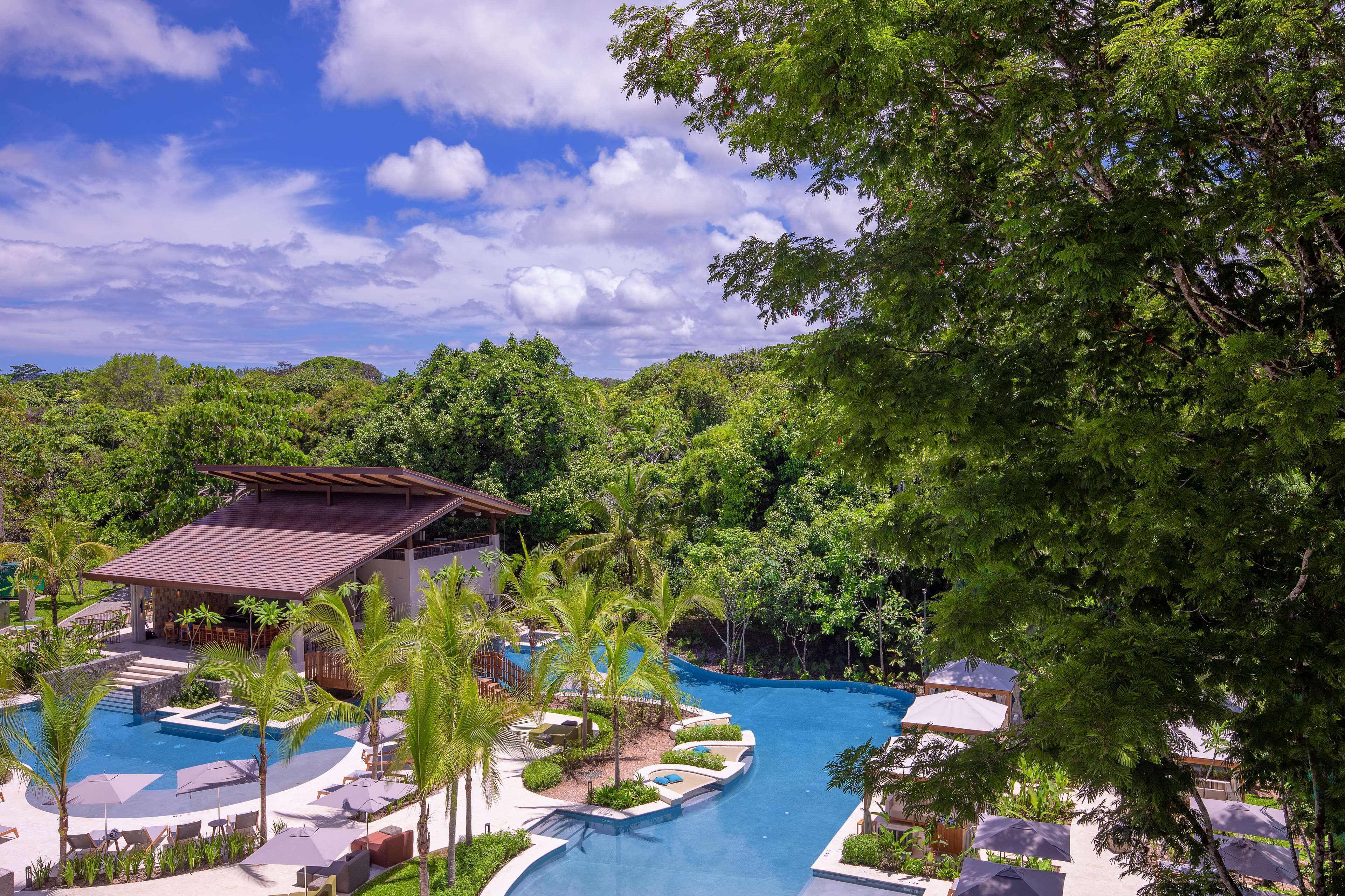A resort with a swimming pool, lounge chairs, and a building with a roof.