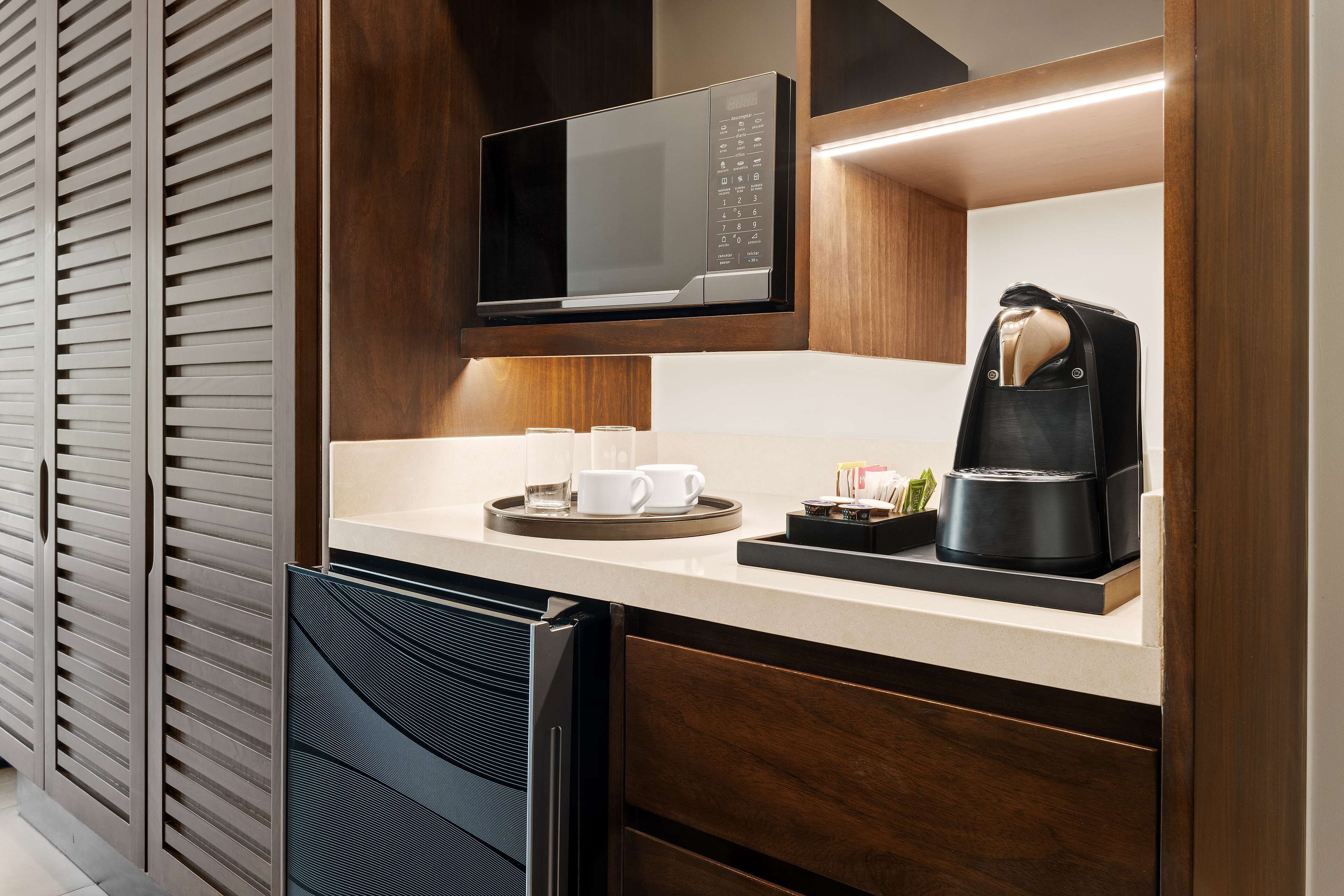A modern kitchen with a built-in microwave, coffee maker, and a tray with cups and a small plant.