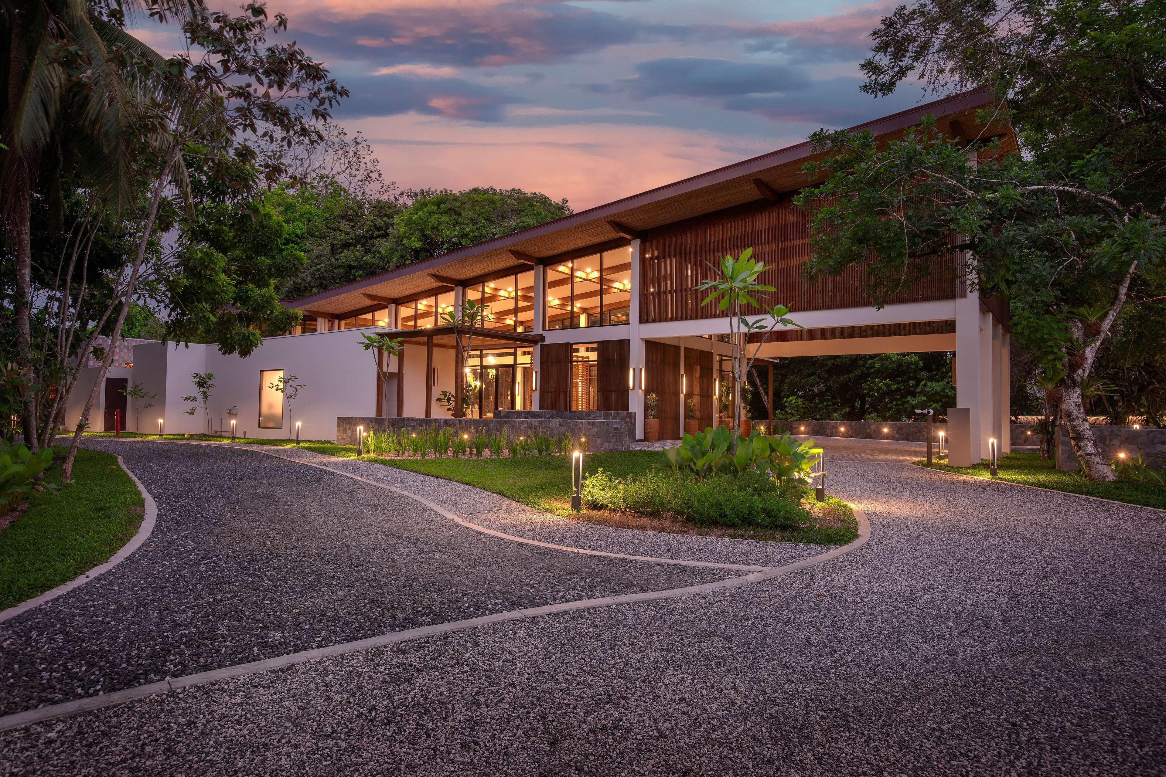 A modern building with a gravel driveway and surrounding greenery.