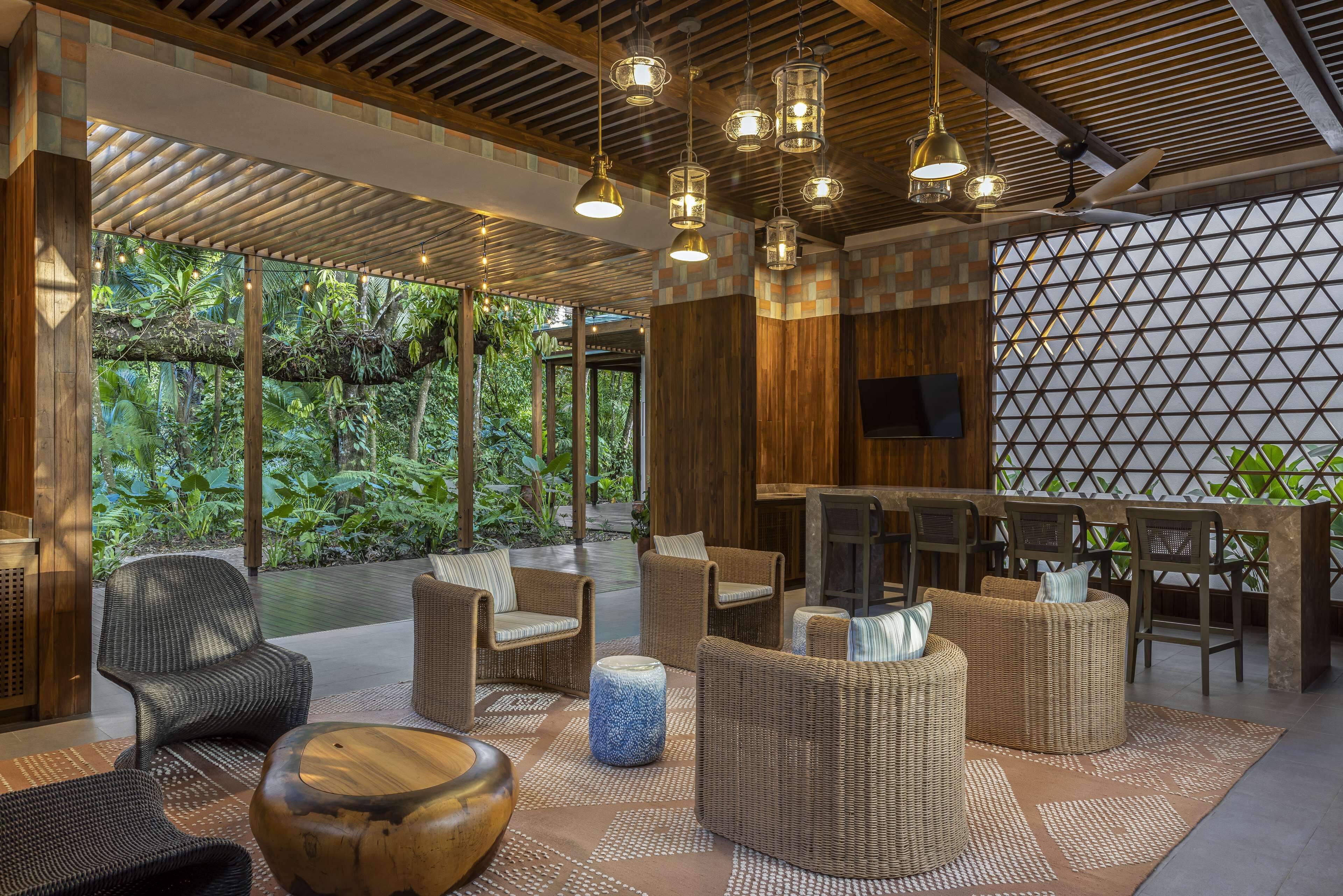 A modern lounge area with wicker furniture, a wooden ceiling, and a view of lush greenery.