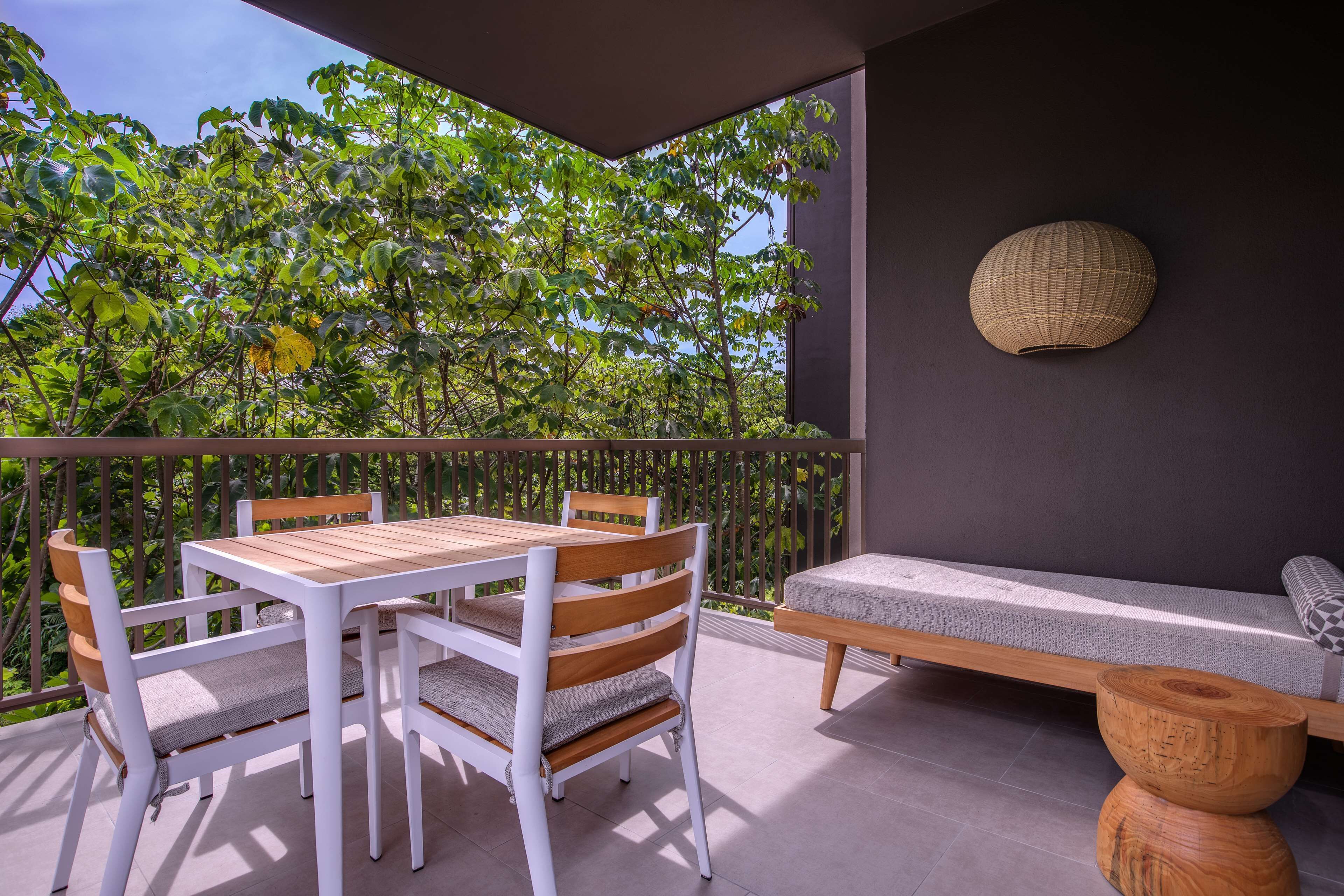 Un balcon avec une table et des chaises en bois, un canapé et une décoration murale en fibres tressées.