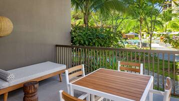 Varanda com mesa e cadeiras de madeira, um sofá e vista para uma piscina e vegetação.