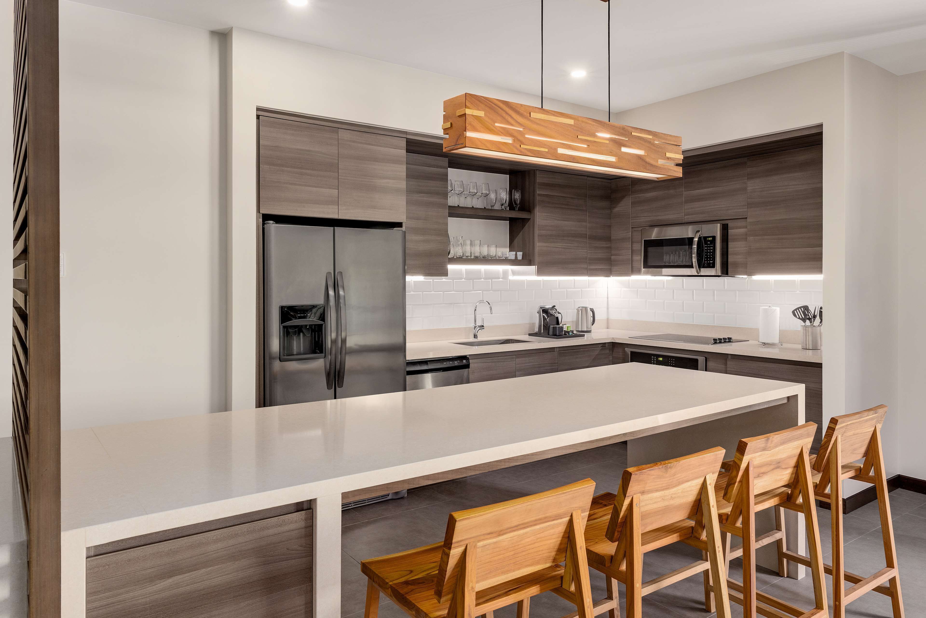 A modern kitchen with a large island, stainless steel appliances, wooden bar stools, and a pendant light.