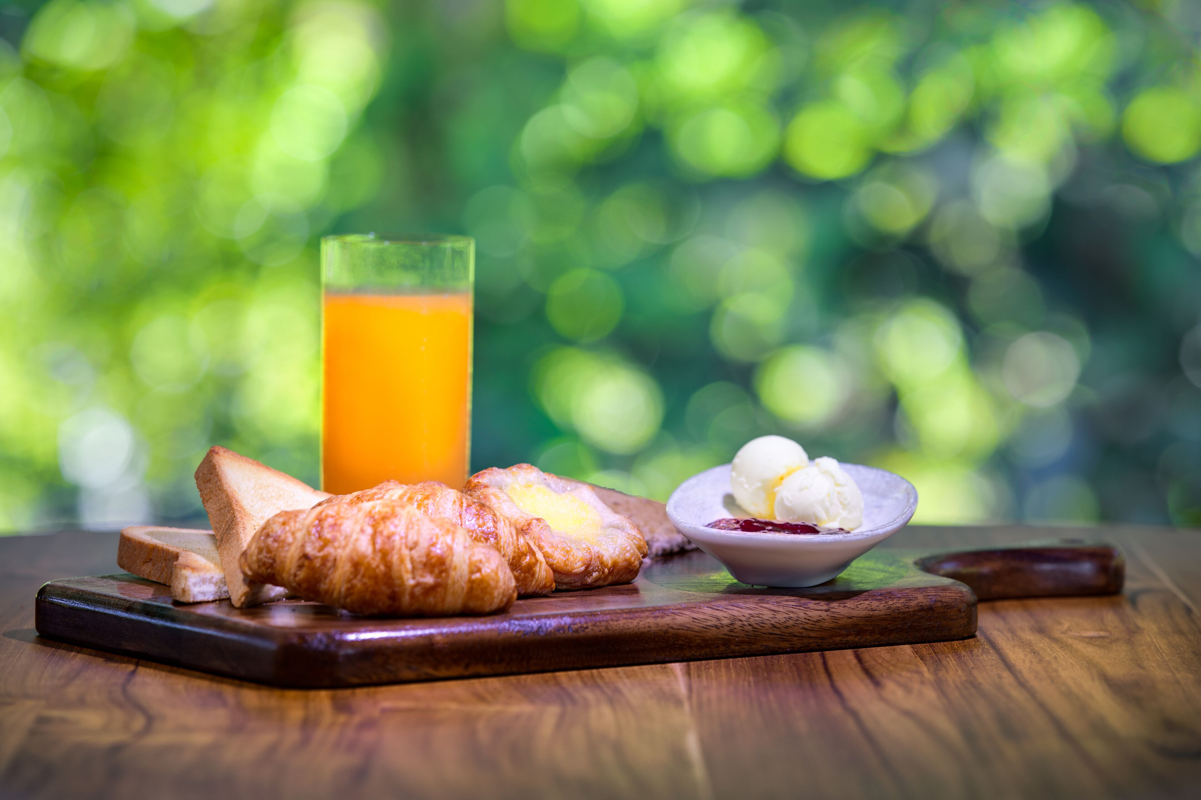A breakfast setting with croissants, a glass of orange juice, and a bowl of ice cream on a wooden table.