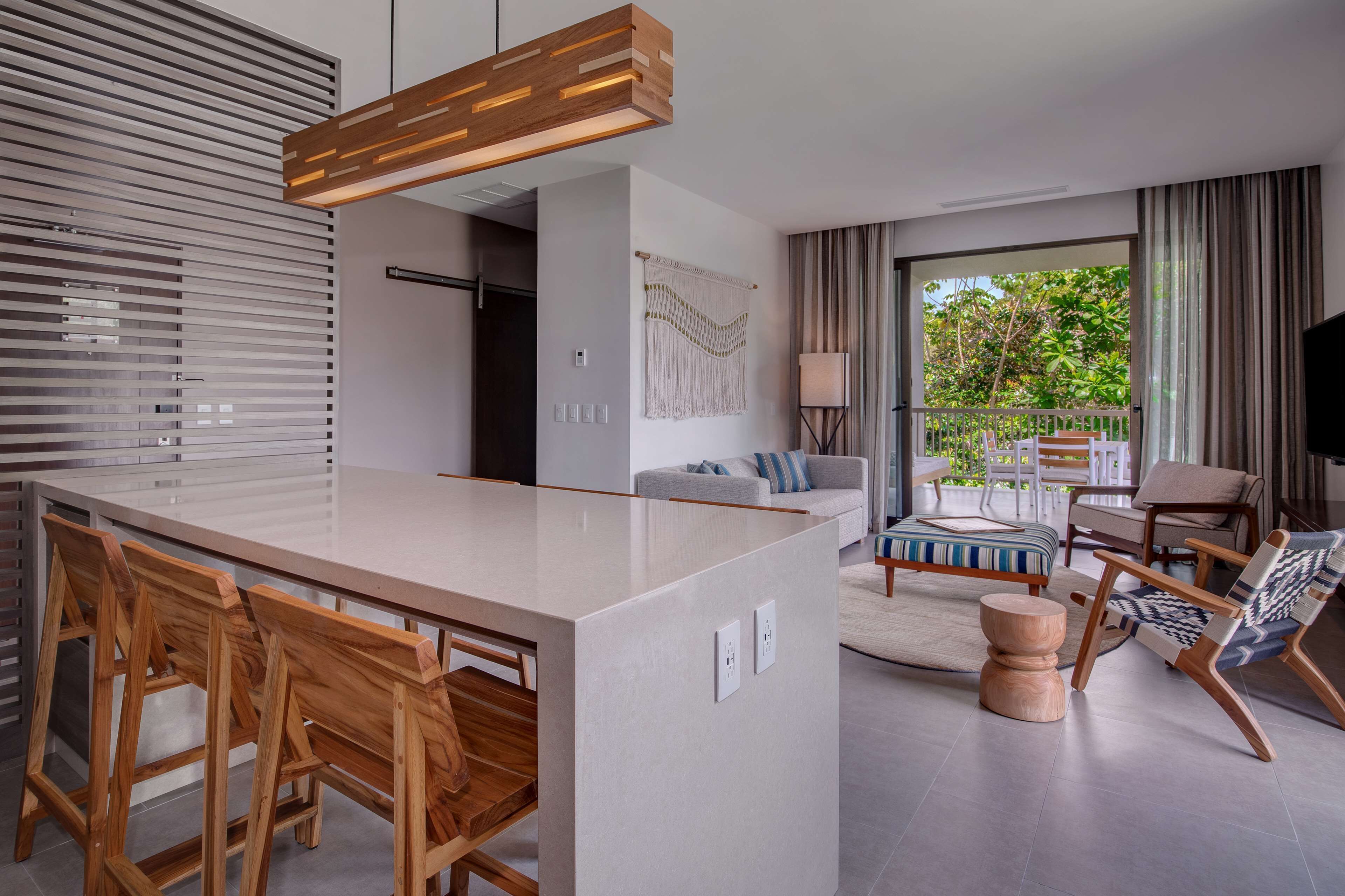 A modern kitchen with a central island, wooden chairs, a sofa, and a view of the outdoors.