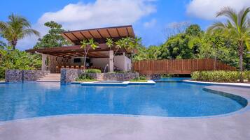 Un área de piscina moderna con una zona de estar cubierta, escalones de piedra y exuberante vegetación tropical.