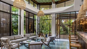 Un espace intérieur spacieux comprenant un ensemble de canapés, des fauteuils et une table basse. De grandes fenêtres offrent une vue sur la verdure environnante.
