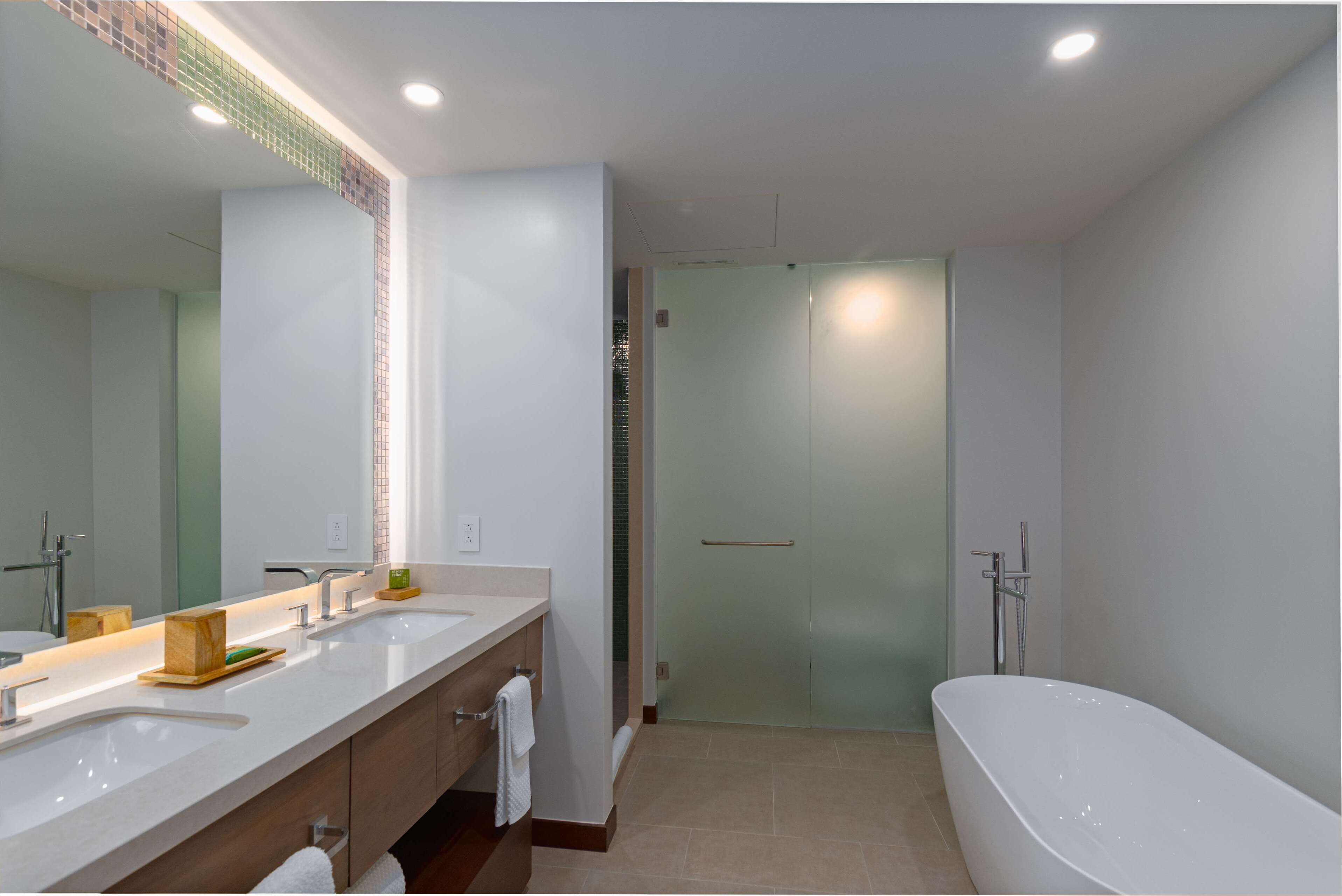 A modern bathroom with two sinks, a large mirror, a bathtub, and a glass shower enclosure.