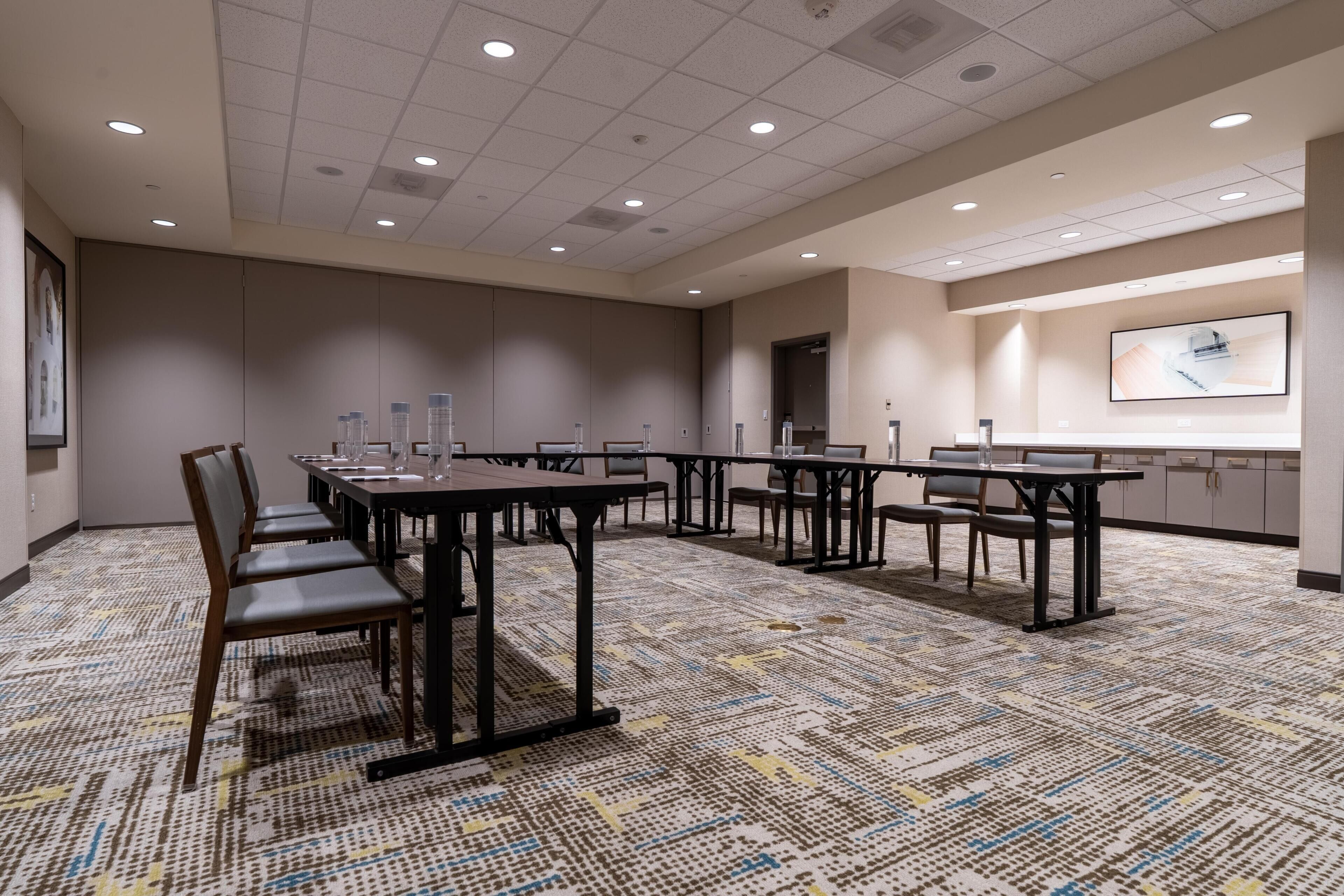 A conference room with multiple tables and chairs, a patterned carpet, and a large screen on the wall.