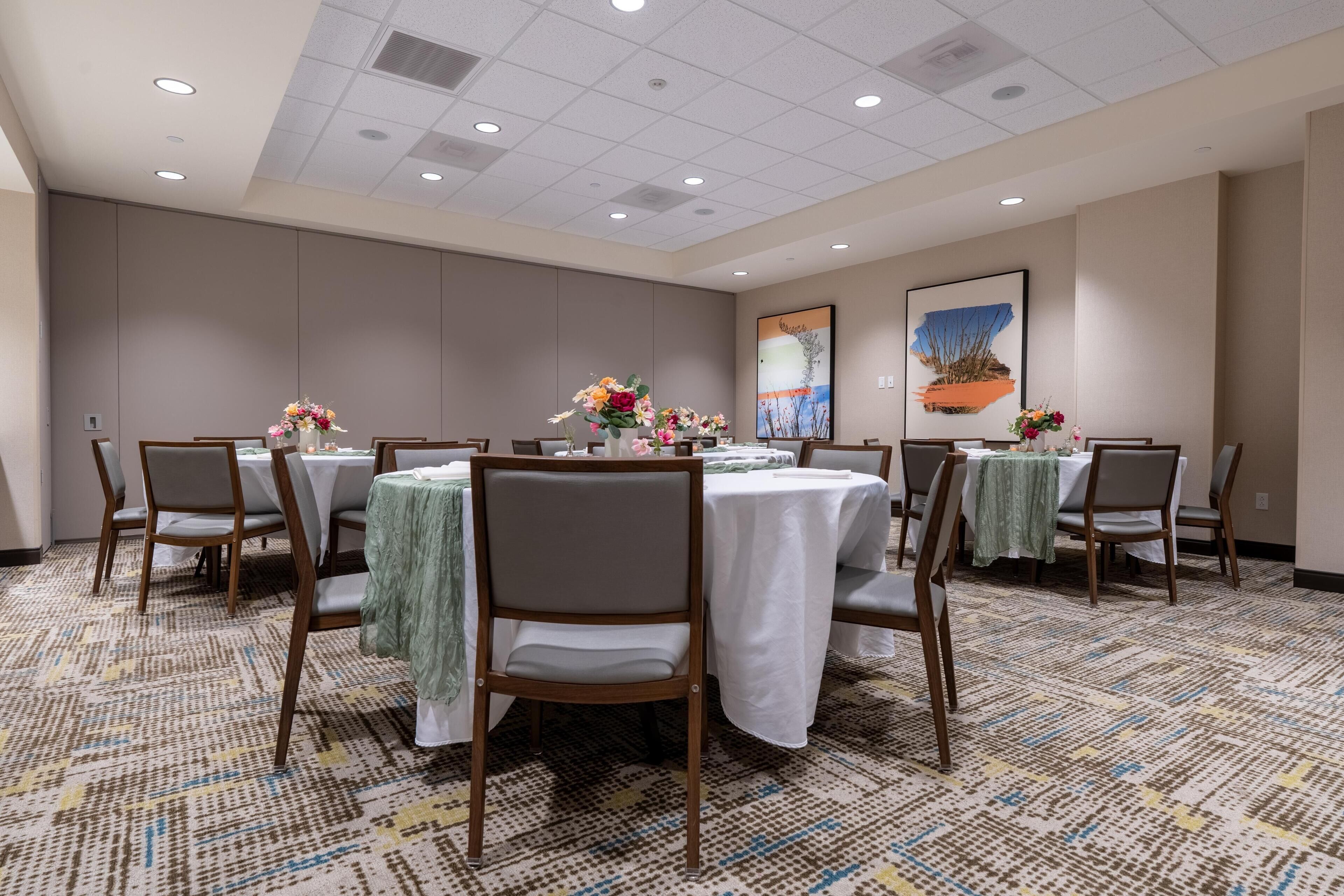 A conference room with tables, chairs, floral centerpieces, and a large painting on the wall.