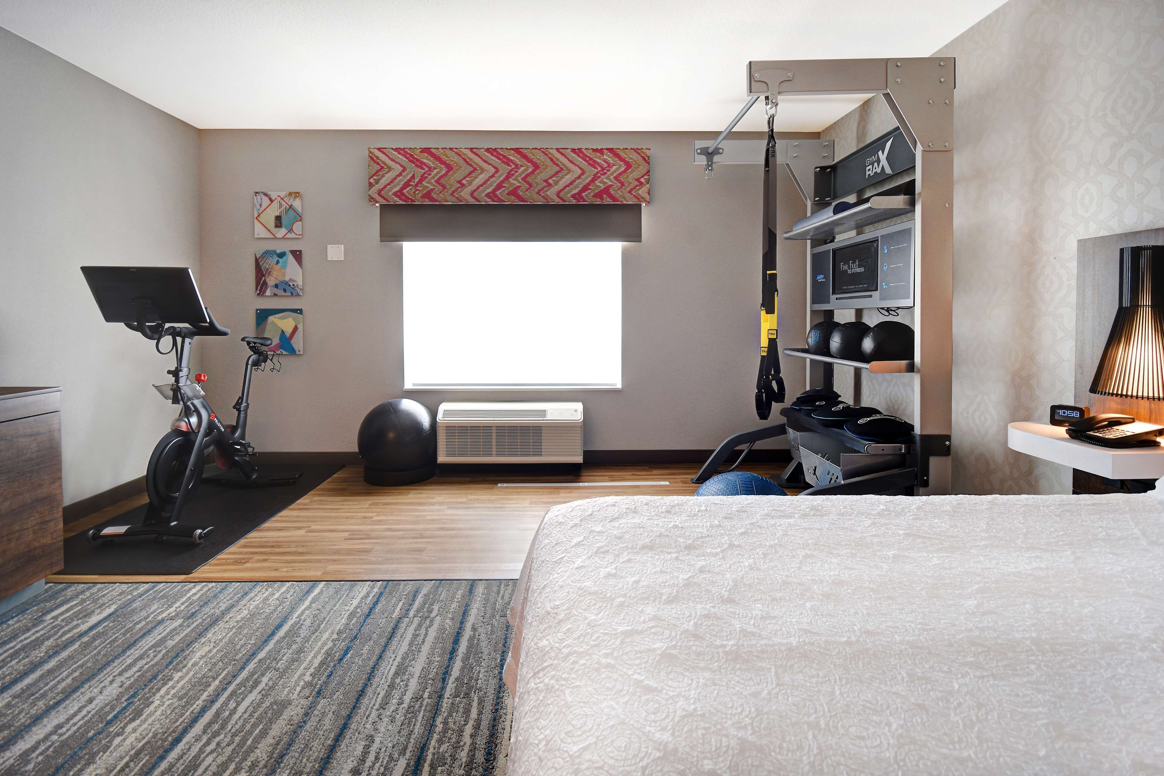 A modern bedroom with a bed, exercise equipment, a desk, and a large window.
