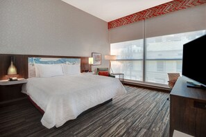 A hotel room with a large bed, a desk, a chair, a TV, a window with a view, and a patterned ceiling.