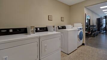 A laundry facility with multiple washers and dryers, a control panel, and a mirror.