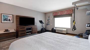 A hotel room with a large bed, a TV, a desk, a bike, and a window with a view.