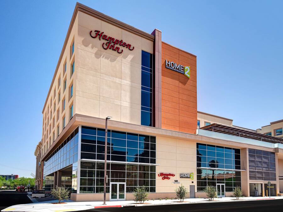 Un hotel Hampton Inn con una fachada moderna, amplias ventanas de vidrio y un llamativo letrero 'HOME2'.