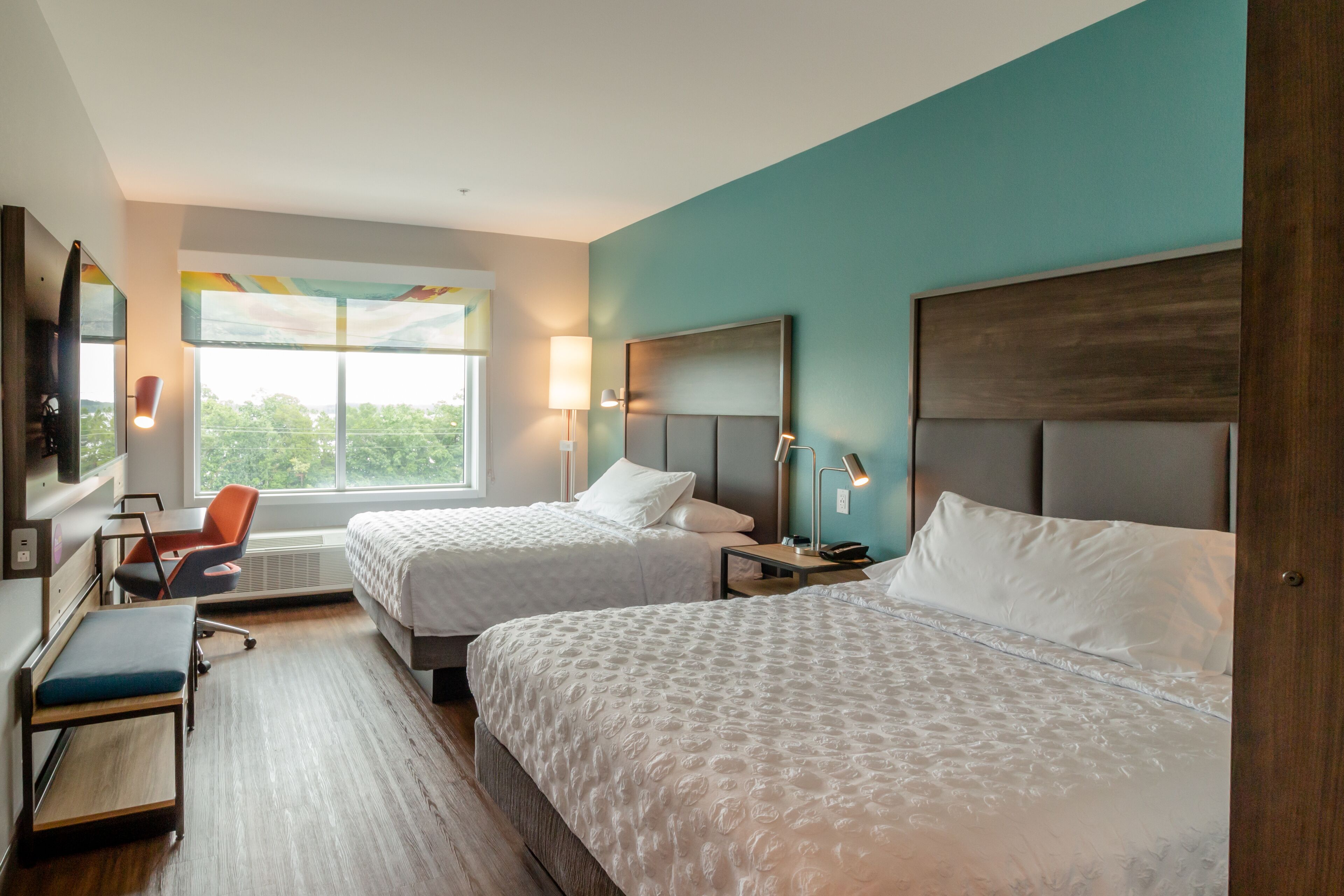 A hotel room with two beds, a desk, a chair, and a large window.