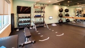 Ein Fitnessraum mit Trainingsgeräten, einem Fernseher und einem Spiegel.