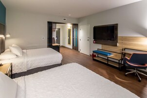 Habitación de hotel con dos camas, un escritorio, una silla, un televisor y un espejo.