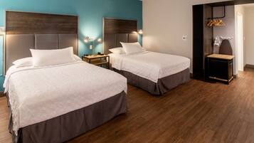 A hotel room with two beds, wooden flooring, and a small seating area with a table and chairs.