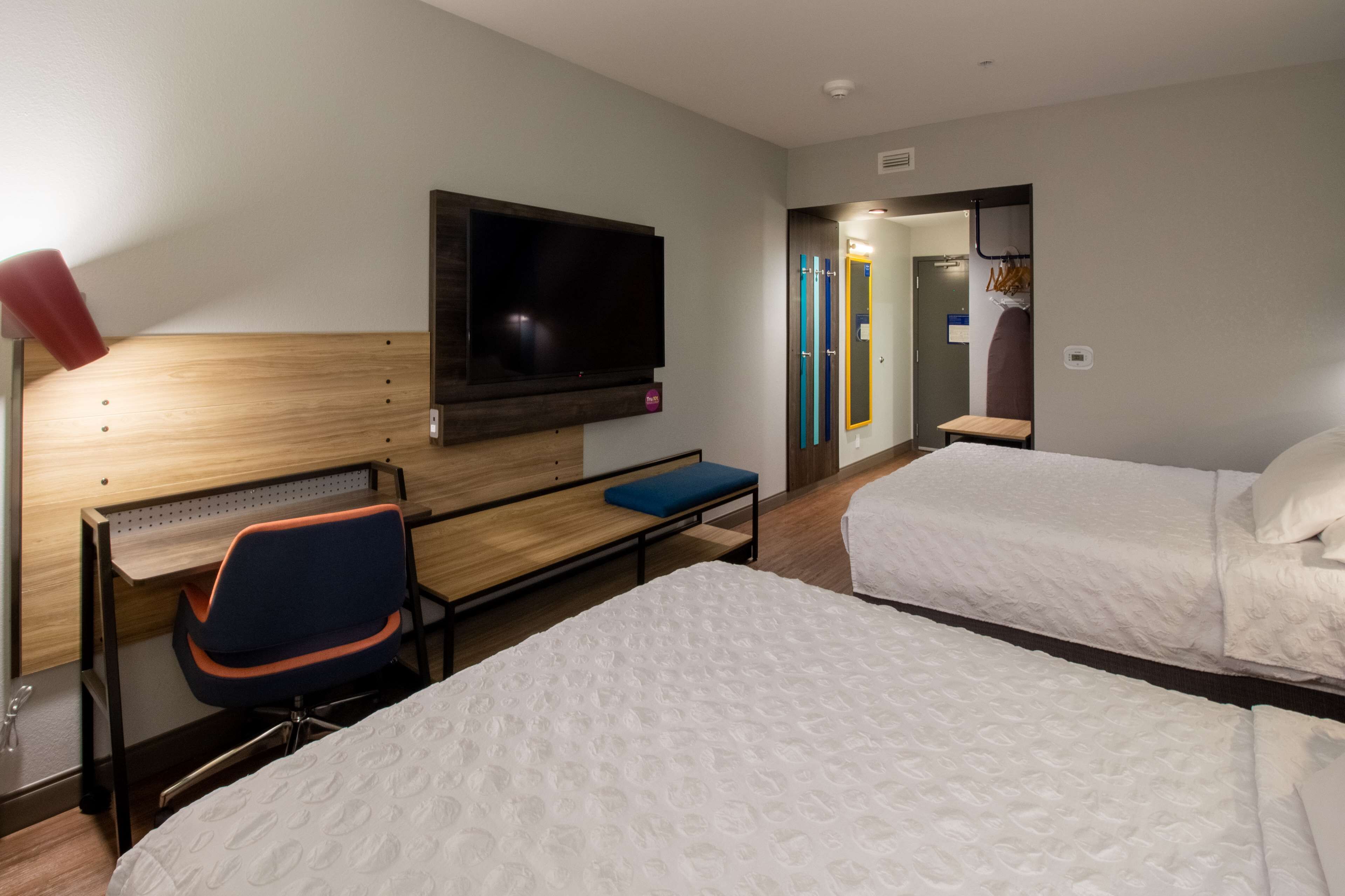 A hotel room with a bed, a desk with a chair, a TV mounted on the wall, and a bathroom visible through an open door.