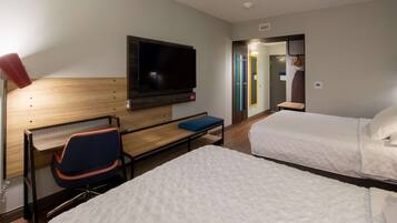 A hotel room with a bed, a desk with a chair, a TV mounted on the wall, and a bathroom visible through an open door.