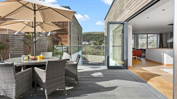 An outdoor dining area with a table and chairs, a large umbrella, and a view of the surrounding landscape. - Close To The Beach,Wi-Fi, Parking (Challaborough)