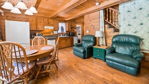 A wooden cabin interior with a dining table, chairs, a sofa, and a staircase.
