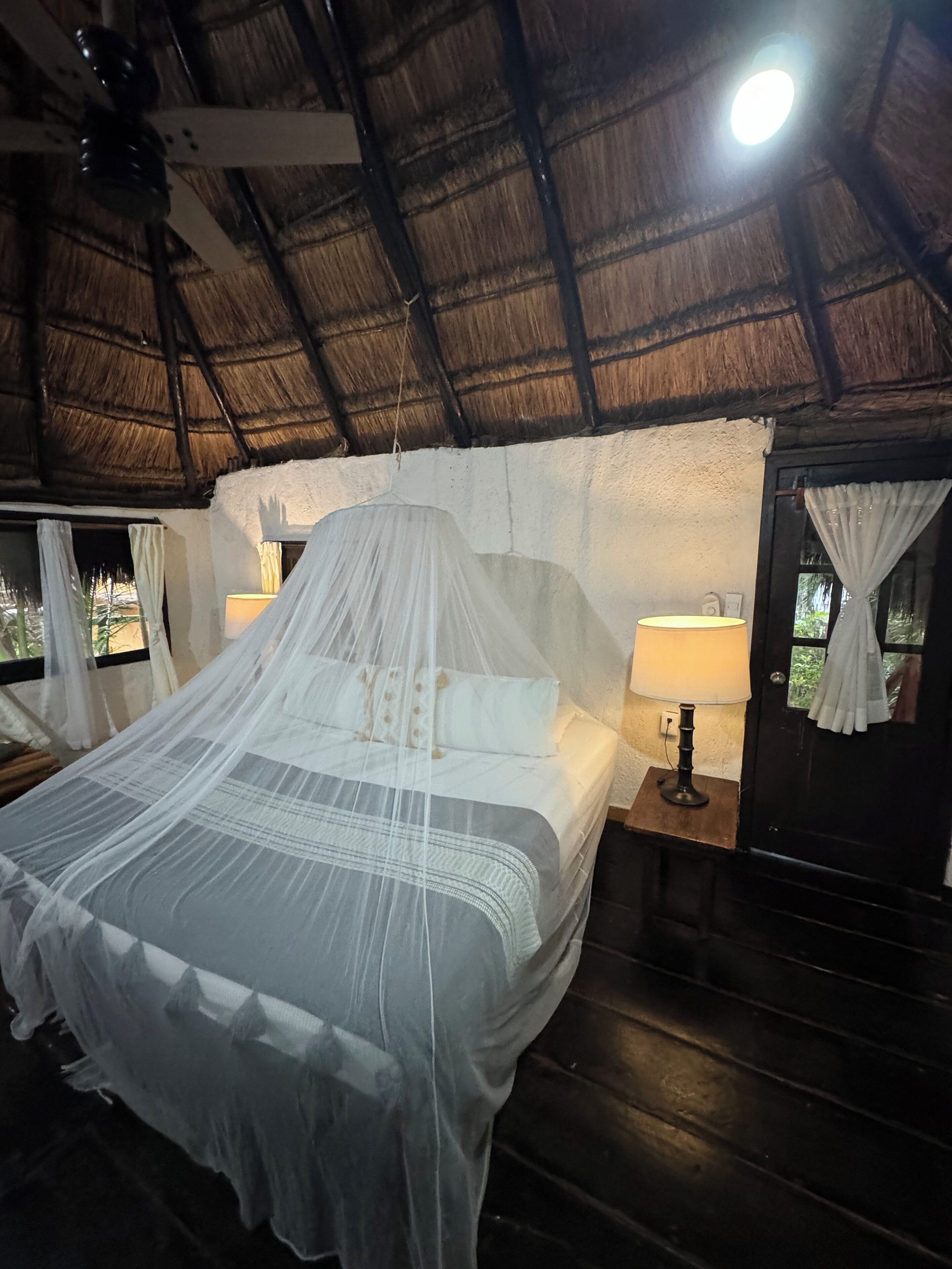 A bed with a mosquito net, a bedside lamp, and a wooden nightstand.