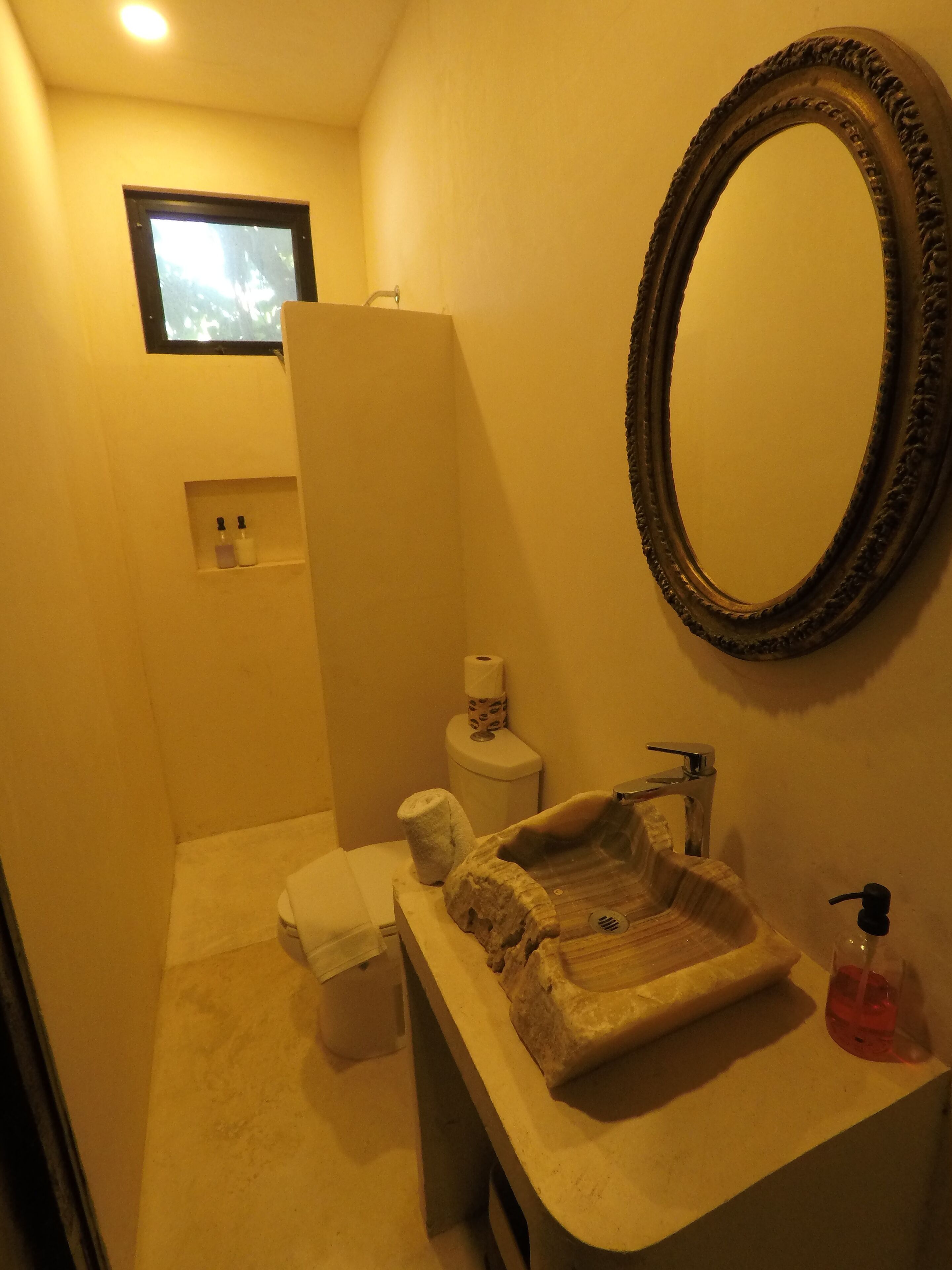 A bathroom with a sink, mirror, toilet, and a small shelf with toiletries.