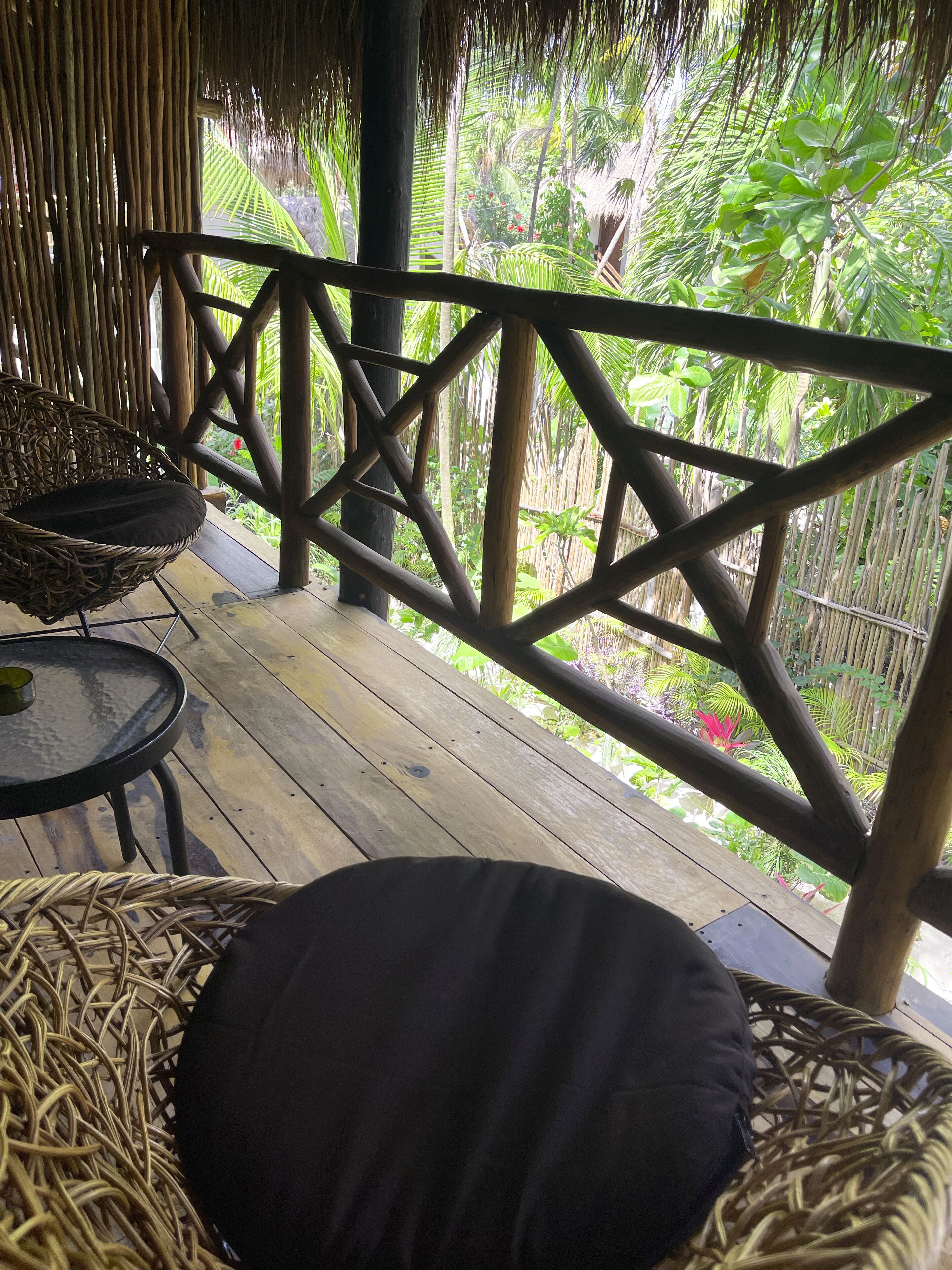 A wooden deck with wicker furniture and a thatched roof structure.
