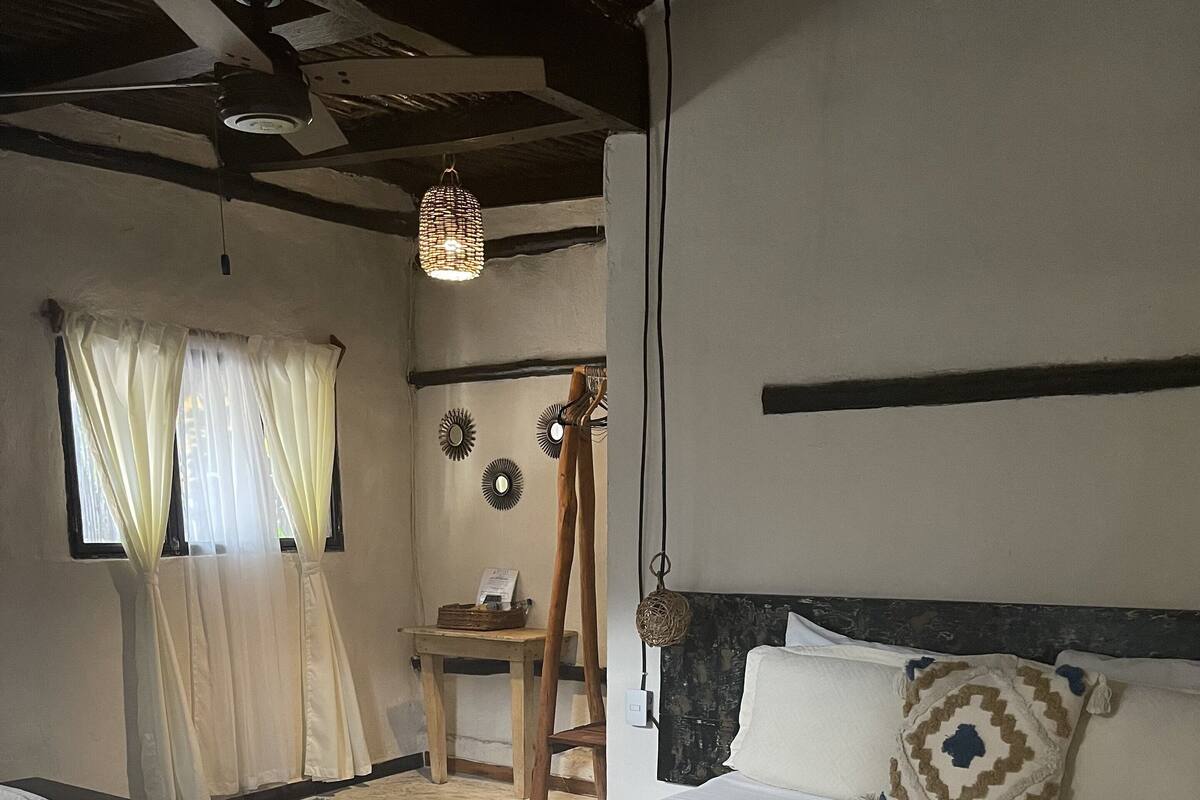 A bedroom with a large bed, a wooden chair, a small table, and a hanging light fixture.