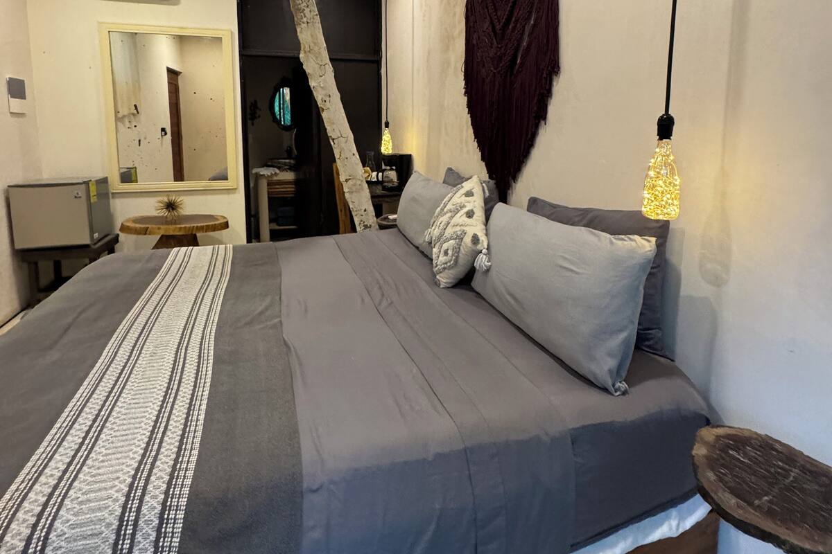 A bedroom with a bed, a ceiling fan, a hanging light fixture, and a mirror.
