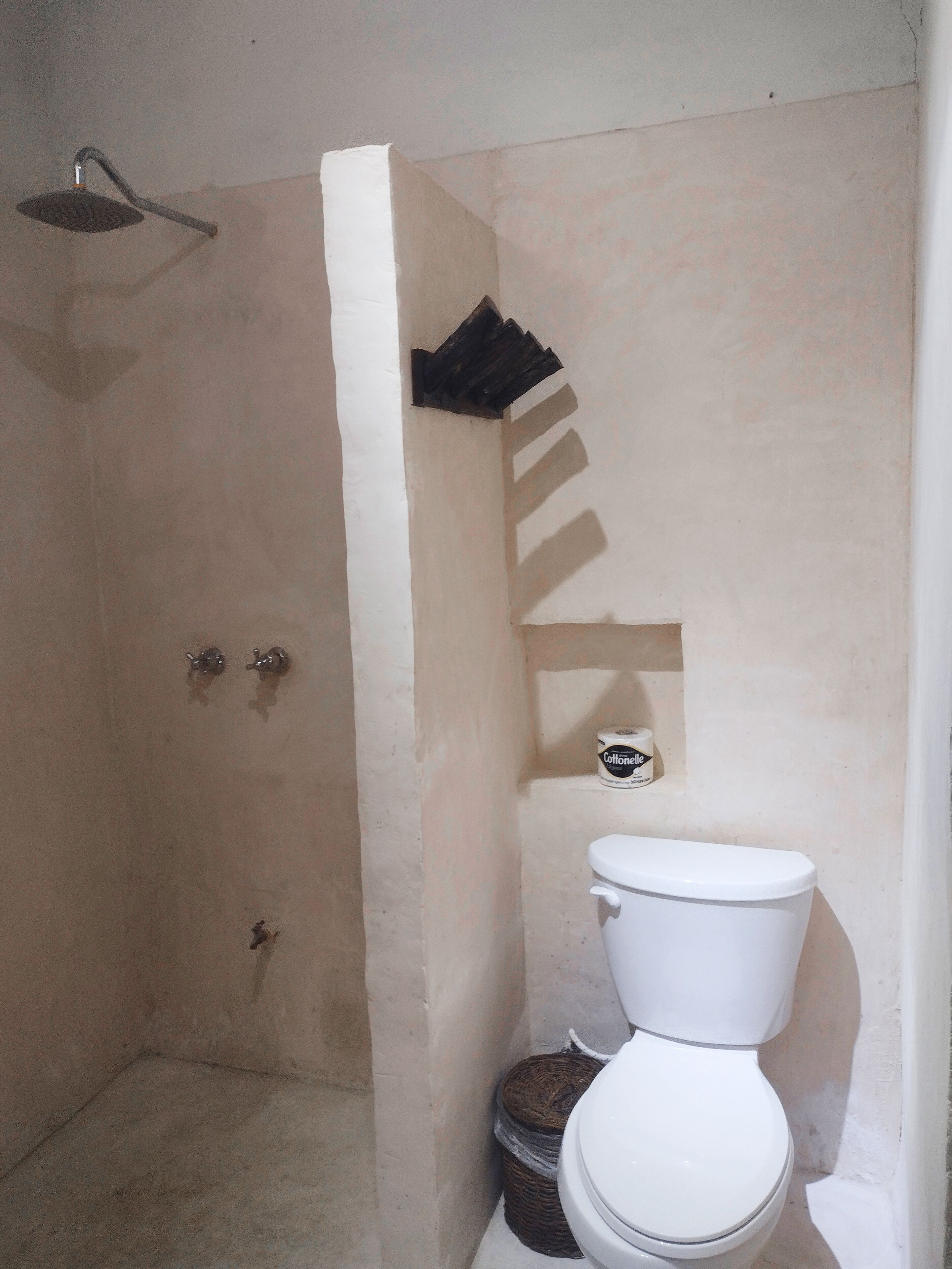 A small, compact bathroom with a shower, toilet, and a small trash bin.